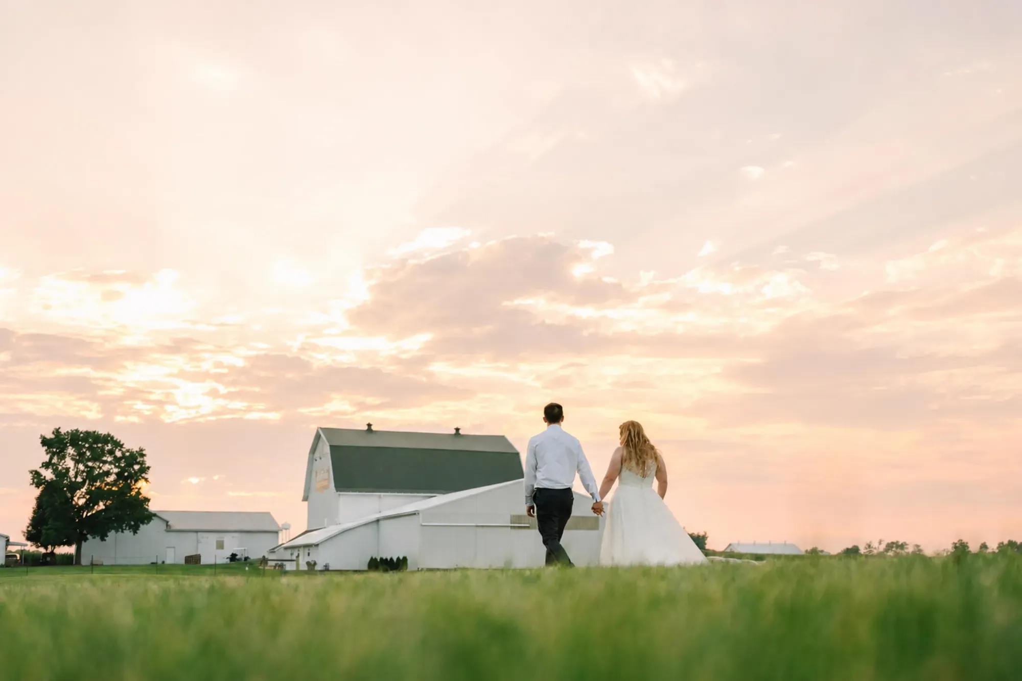 Barn ceremony space with wooden pews, floral aisle markers, and a crystal chandelier